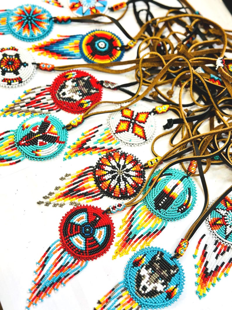 May include: A collection of beaded necklaces featuring colourful geometric patterns and fringe. The necklaces are made with turquoise, red, yellow, black and white beads.
