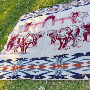 May include: A white throw blanket with a geometric pattern in shades of blue, brown, and red. The blanket features a repeating design of stylized wolves and a Native American inspired pattern.