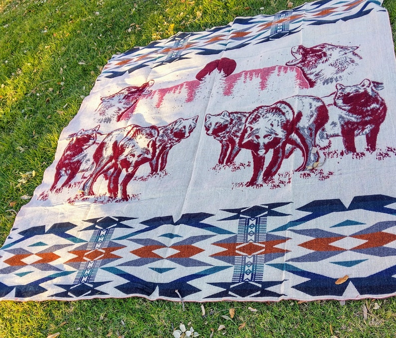 May include: A white throw blanket with a geometric pattern in shades of blue, brown, and red. The blanket features a repeating design of stylized wolves and a Native American inspired pattern.