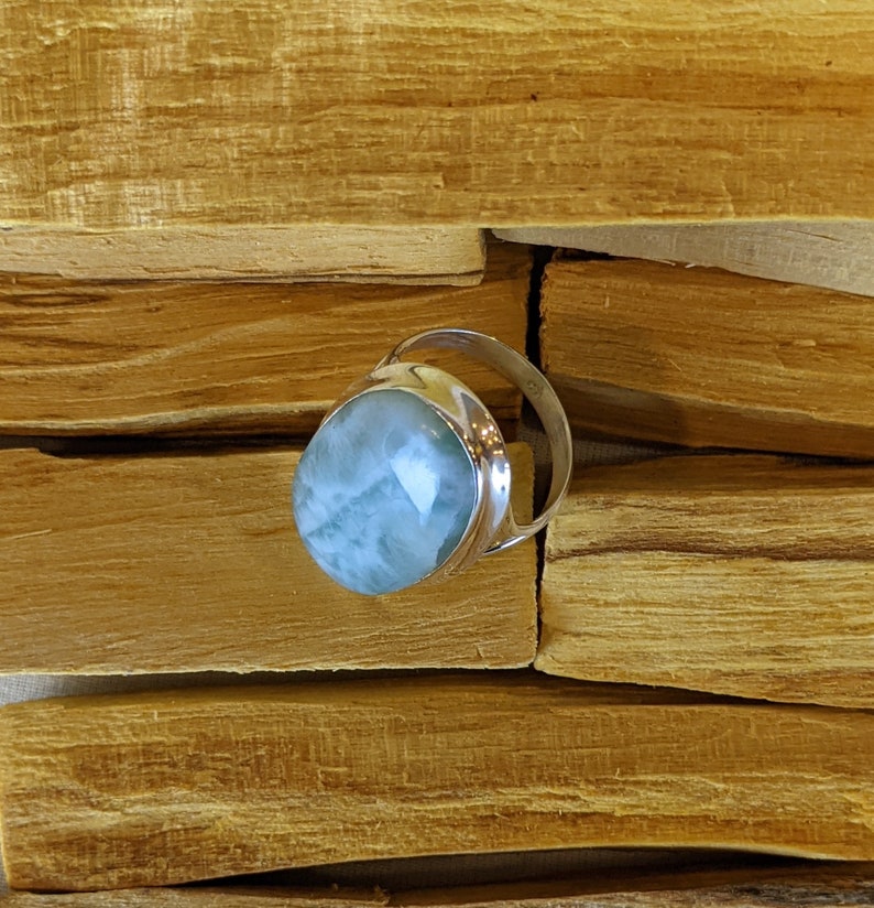May include: A silver ring featuring a light blue oval-shaped gemstone. The ring is displayed on a wooden surface.