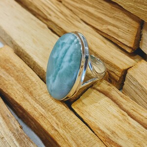 May include: A silver ring featuring a large oval-shaped blue and green gemstone. The ring is displayed on a wooden surface.