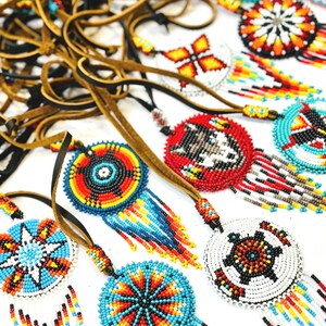 May include: A collection of beaded Native American dreamcatchers with colourful geometric patterns and fringe. The dreamcatchers are strung on brown leather cords.