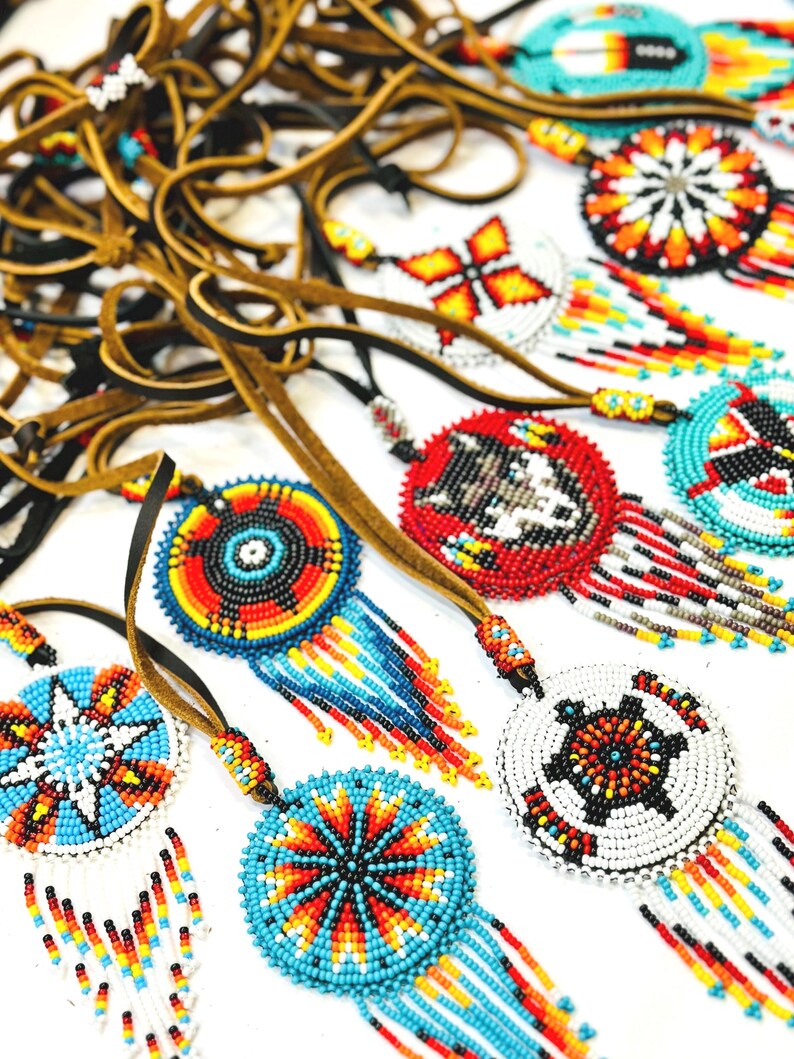 May include: A collection of beaded Native American dreamcatchers with colourful geometric patterns and fringe. The dreamcatchers are strung on brown leather cords.