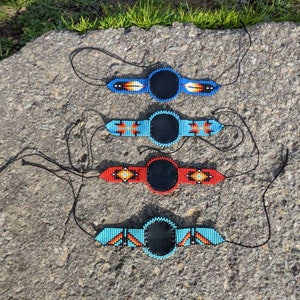 May include: Four beaded necklaces with black round pendants. The necklaces are in different colors, including blue, red, and turquoise.