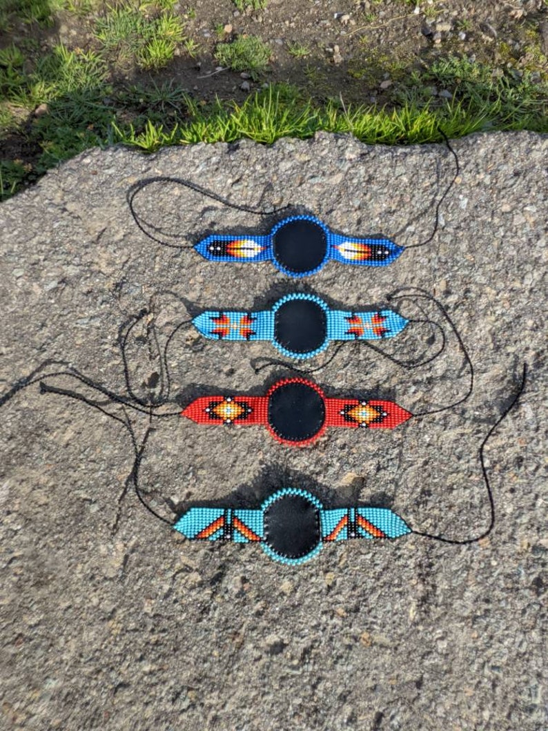 May include: Four beaded necklaces with black round pendants. The necklaces are in different colors, including blue, red, and turquoise.