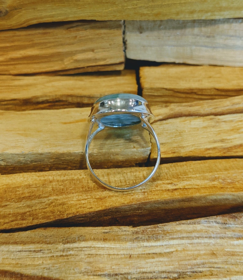 May include: A silver ring featuring a large, oval-shaped, light blue gemstone. The ring is displayed on a wooden surface.