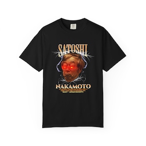 Op de afbeelding: Zwart t-shirt met een afbeelding van een mannengezicht met rood oplichtende ogen, de naam "SATOSHI" erboven en "NAKAMOTO" eronder. Het shirt bevat een citaat: "IF YOU DON'T BELIEVE ME OR DON'T GET IT..."