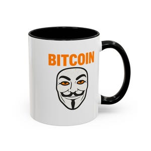 Puede incluir: Taza de cerámica blanca con interior y asa negros. La taza presenta la palabra "BITCOIN" en letras naranjas sobre una máscara estilizada con ojos naranjas y bigote.