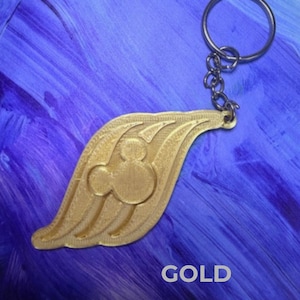 May include: Gold-colored keychain featuring a stylized wing design with a Mickey Mouse silhouette in the center. The word "GOLD" is printed in white. The keychain includes a metal ring and chain for attaching keys.