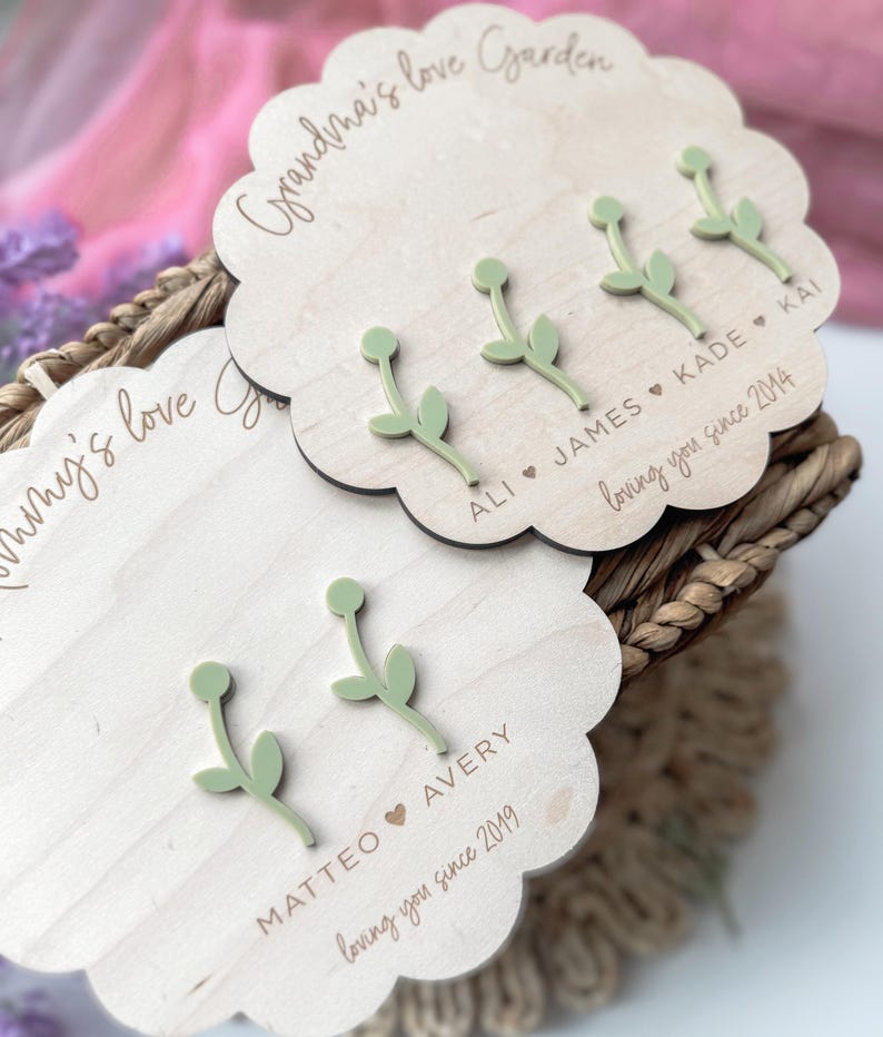 Op de afbeelding: Drie houten plaquettes met de tekst "Grandma's love Garden", "ALI JAMES KADE KAI loving you since 2014" en "MATTEO AVERY loving you since 2019". Elke plaquette heeft een groene houten bloem.