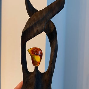Könnte beinhalten: Eine dunkelbraune Holzskulptur mit einem einzigartigen, abstrakten Design. Die Skulptur verfügt über eine kreisförmige Öffnung, in der sich ein kleiner, bernsteinfarbener Edelstein befindet.