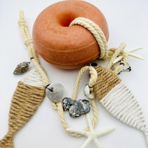 Könnte beinhalten: Eine Sammlung maritimer Dekorationen. Im Mittelpunkt steht eine runde, orangefarbene Boje mit einem Seil. Dazu kommen dekorative Fischformen mit Seil umwickelt, Muscheln und ein weißer Seestern.