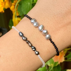 May include: Two bracelets on a wrist. One bracelet is black with white pearls, the other is white with black pearls.