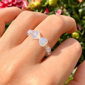 May include: A ring made of white heart-shaped beads. The ring is on a person's finger.