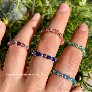 May include: Five gemstone rings with silver beads. The rings are stacked on a finger and feature amethyst, carnelian, lapis lazuli, and two shades of blue turquoise.