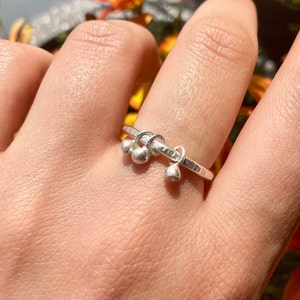 Könnte beinhalten: Ein silberner Ring mit drei baumelnden Kugeln. Der Ring ist texturiert und hat eine gehämmerte Oberfläche.