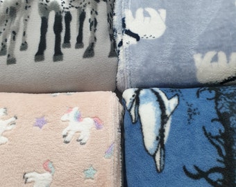 May include: Four different plush blankets with various animal prints. The first blanket is gray with a black and white zebra print. The second blanket is light blue with a white polar bear print. The third blanket is pink with a white unicorn print and white stars. The fourth blanket is blue with a white dolphin print and black tree branches.