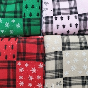 May include: Four folded Christmas-themed blankets. The blankets feature a patchwork design with plaid patterns in green, pink, red, and beige. Each blanket square is decorated with white snowflakes, Christmas trees, and bells.