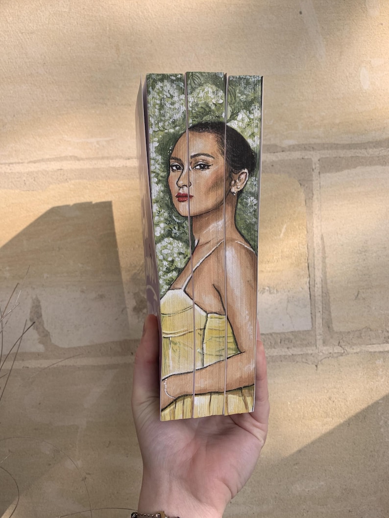 Pode incluir: Uma obra de arte pintada &agrave; m&atilde;o com um retrato de uma mulher com cabelo escuro e batom vermelho, vestindo um vestido amarelo. O fundo tem um design floral verde e branco. A obra de arte est&aacute; em uma superf&iacute;cie de madeira.