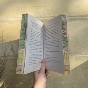 Pode incluir: Um livro aberto com texto impresso e ilustra&ccedil;&otilde;es, segurado por uma m&atilde;o. As p&aacute;ginas do livro s&atilde;o brancas e a capa apresenta um design verde e branco. As ilustra&ccedil;&otilde;es parecem ser de uma pessoa. O livro est&aacute; aberto, revelando o texto.