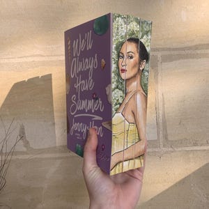 Pode incluir: Um livro de capa dura intitulado "We'll Always Have Summer" de Jenny Han. O livro tem uma capa roxa com ilustra&ccedil;&otilde;es e texto. A lateral do livro apresenta um retrato pintado de uma mulher em um vestido amarelo.