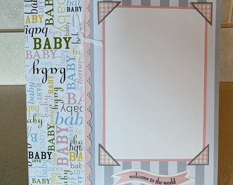 May include: A baby announcement card with a white frame and a pink and gray striped border. The card has a scalloped edge and a banner that says "welcome to the world".