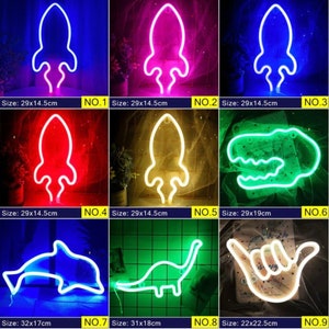 May include: Collection of neon signs in various shapes and colors, including a rocket, dinosaur, dolphin, and hand gesture. Each sign is illuminated with vibrant colors like blue, pink, red, and green. Sizes vary, with the rocket signs measuring approximately 11.4 x 5.7 inches.