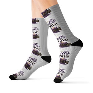 May include: Gray socks with black heels and toes, featuring a repeating pattern of a purple candle with the text "BN" and "ells sive". The socks have a crown graphic and star accents.