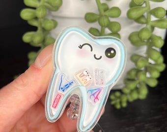 May include: A blue and white cartoon tooth with a smiling face and a winking eye. The tooth is filled with dental tools and supplies, including a toothbrush, toothpaste, floss, and a dental mirror. The tooth is attached to a clear plastic retractable badge holder.
