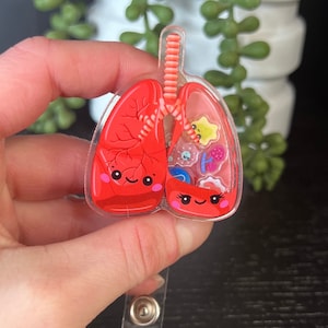 May include: A red and clear plastic badge holder with a cartoon image of lungs. The lungs have a smiling face and are filled with colorful glitter and small cartoon images.