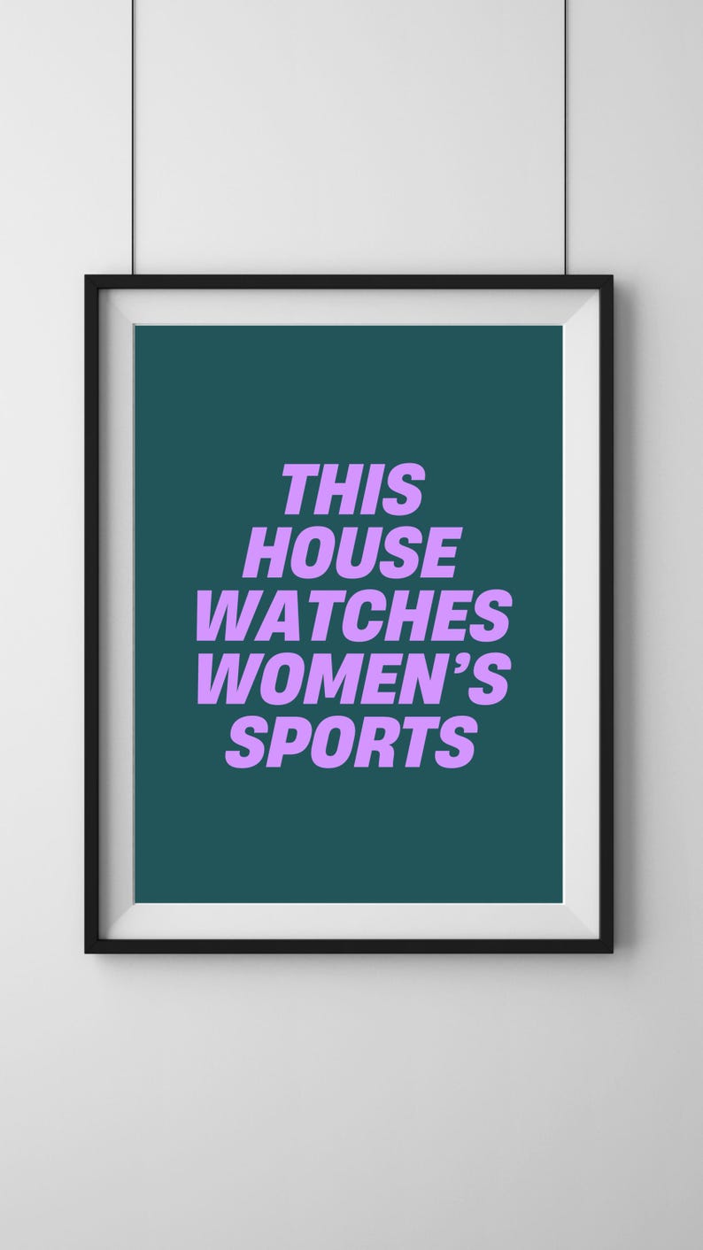 Pode incluir: Uma impress&atilde;o emoldurada com fundo azul-esverdeado e texto branco que diz "This house watches women's sports" em roxo.