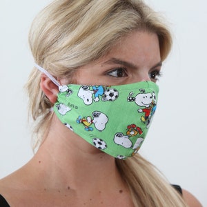 May include: A green face mask with a white elastic band. The mask has a repeating pattern of cartoon dogs playing soccer. The text "UFS" is visible on the mask.