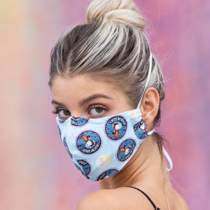 May include: A woman wearing a blue face mask with a white background and a pattern of cartoon characters. The mask has the text "I Need My Space" on it.