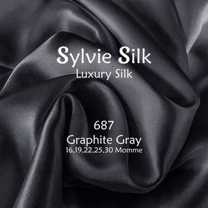 May include: Close-up of a dark gray silk fabric with the text "Sylvie Silk Luxury Silk 687 Graphite Gray 16,19,22,25,30 Momme" printed on it.
