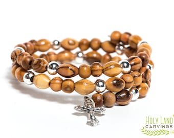 May include: A triple-strand bracelet made of olive wood beads with silver accents and a silver cross charm. The bracelet is a religious item and is perfect for everyday wear.