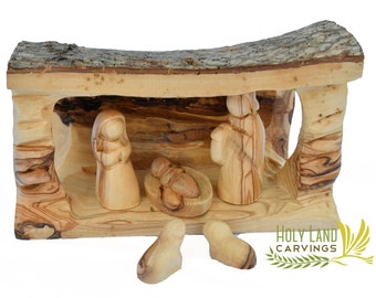 May include: A wooden nativity scene carved from olive wood. The scene includes figures of Mary, Joseph, baby Jesus in a manger, and two animals. The figures are set inside a wooden stable with a bark roof.