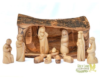 May include: A nativity scene carved from olive wood. The figures include Mary, Joseph, baby Jesus, a shepherd, and two sheep. The scene is set in a hollowed-out log, which serves as the stable.