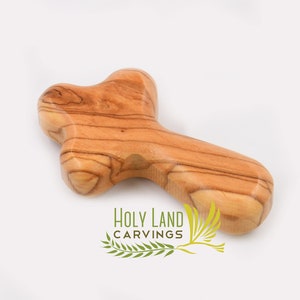 May include: A small, wooden cross made from olive wood. The cross is a light brown color with a natural wood grain. It is a simple, yet beautiful, religious symbol.