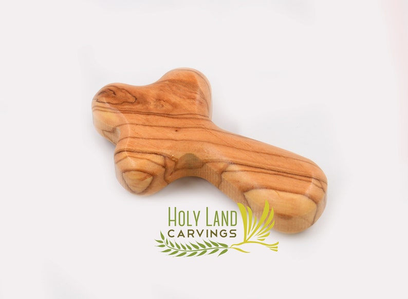 May include: A small, wooden cross made from olive wood. The cross is a light brown color with a natural wood grain. It is a simple, yet beautiful, religious symbol.