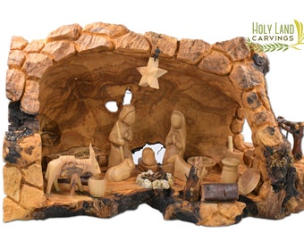 May include: A hand-carved nativity scene set in a hollowed-out olive wood log. The figures include Mary, Joseph, baby Jesus, a donkey, a sheep, and a star. The scene is decorated with small details like a fire, a basket, and a wooden fence.