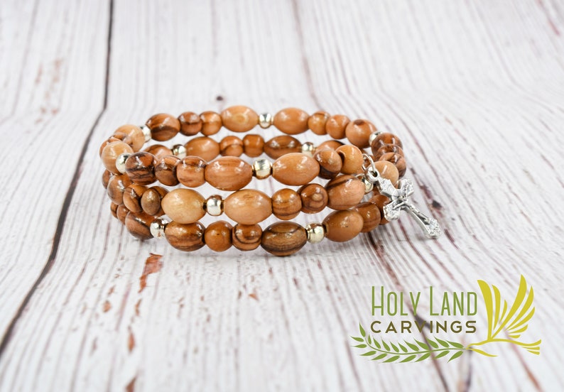 May include: A triple-strand olive wood bracelet with a silver cross charm. The bracelet is made of natural wood beads and has a rustic look.