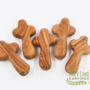 May include: Five small wooden crosses made from olive wood. The crosses are a light brown color and have a natural wood grain. The crosses are all different shapes and sizes.