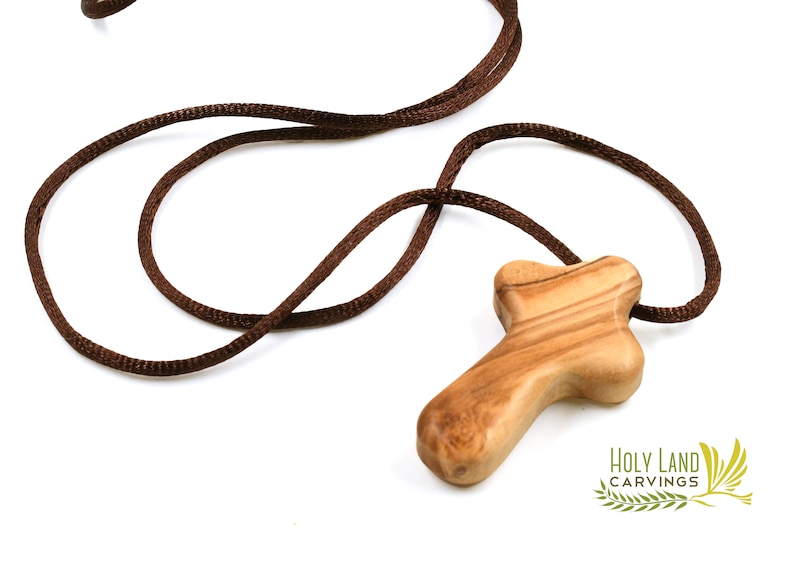 Puede incluir: Un colgante de cruz de madera marr&oacute;n con un cord&oacute;n marr&oacute;n. La cruz est&aacute; hecha de madera de olivo y tiene un dise&ntilde;o simple y r&uacute;stico. El cord&oacute;n mide aproximadamente 50 cm de largo.