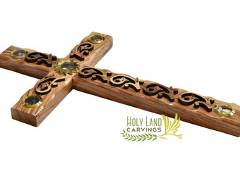 May include: A wooden cross with intricate carvings and gold accents. The cross is decorated with small round glass pieces. The text "HOLY LAND CARVINGS" is visible at the bottom of the cross.
