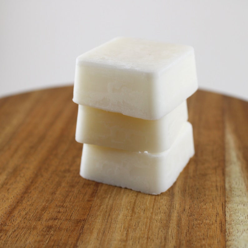May include: Three white square-shaped bars of soap stacked on top of each other on a wooden surface.