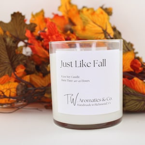 May include: A white soy candle in a clear glass jar with a brown rim. The candle is labeled "Just Like Fall" and has the text "8.5oz Soy Candle, Burn Time: 40-45 Hours, TW. Aromatics & Co., Handmade in Richmond, VA".