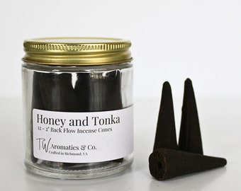 May include: A glass jar with a gold lid filled with black backflow incense cones. The label reads "Honey and Tonka 12 - 2' Back Flow Incense Cones TW Aromatics & Co. Crafted in Richmond, VA". Three cones are shown outside the jar.