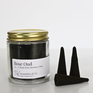 May include: A glass jar filled with black incense cones labeled "Rose Oud 12 - 2" Back Flow Incense Cones TW Aromatics & Co. Crafted in Richmond, VA". Three black incense cones are shown in front of the jar.