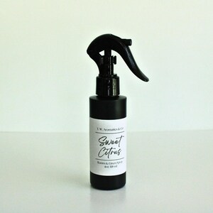 May include: A black room and linen spray bottle with a black spray nozzle. The label reads "Sweet Citrus" and "Room & Linen Spray 4oz 118 ml". The bottle is on a white surface.
