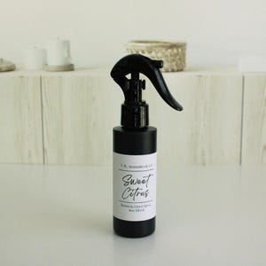 May include: A black room and linen spray bottle with a black trigger. The label reads "Sweet Citrus" and "Room & Linen Spray 4oz 118 ml". The bottle is on a white surface.